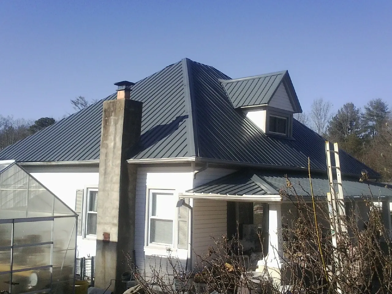 Dark blue standing seam metal roof on a white farmhouse with dormer — Slate & Tile Roof Repair by Roofing Brothers in Colerain