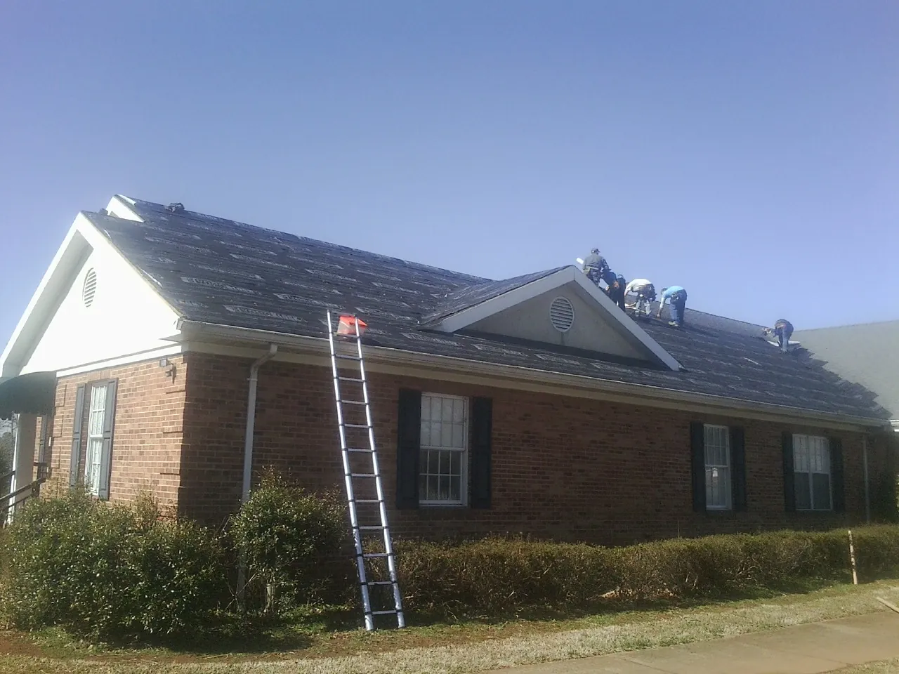 Crew tearing shingles off a brick ranch roof with a ladder set — Metal Roof Repair work by our crew in Colerain