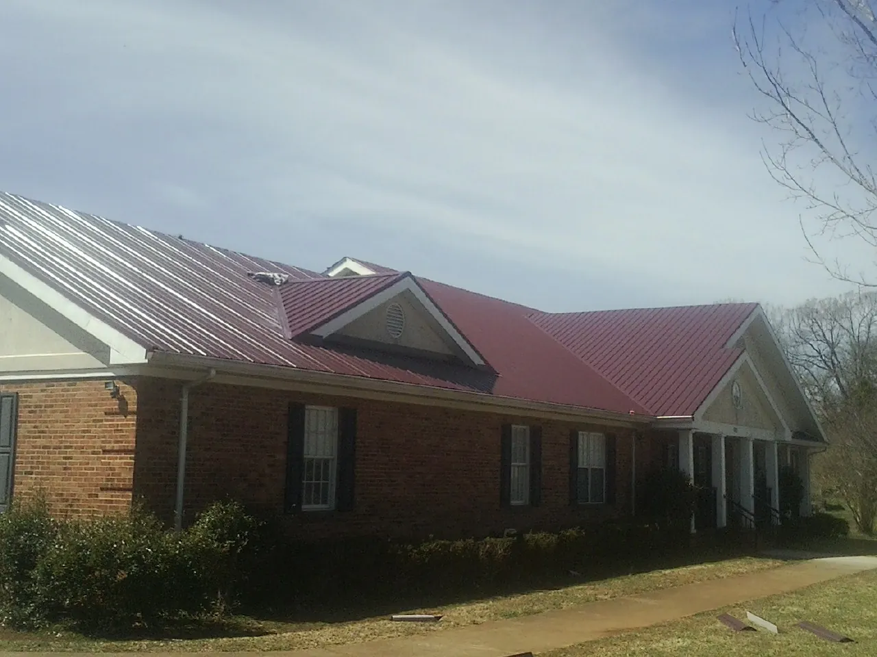 Red metal roof with gabled entries on a long brick building, from a Hail Damage Roof Repair job in Colerain