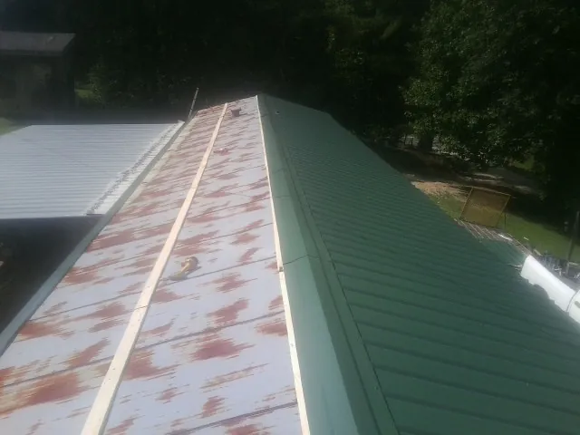 Old rusted panels beside newly installed green metal roofing — Wind Damage Roof Repair by Roofing Brothers in Colerain