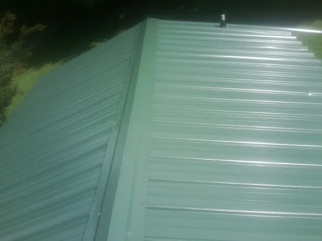 New green metal panels meeting at the ridge of a roof — Flat Roof Repair work by our crew in Colerain