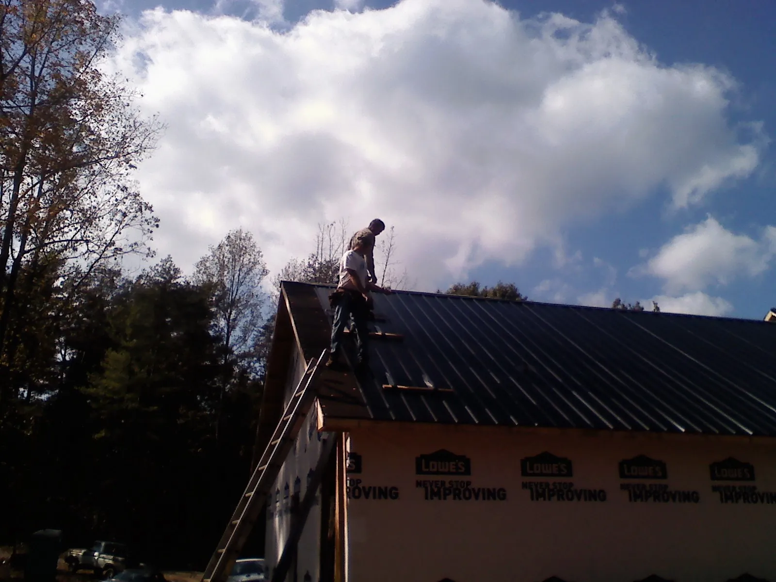 Roofer fastening dark metal panels high against a cloudy sky, from a Roof Inspection job in Colerain