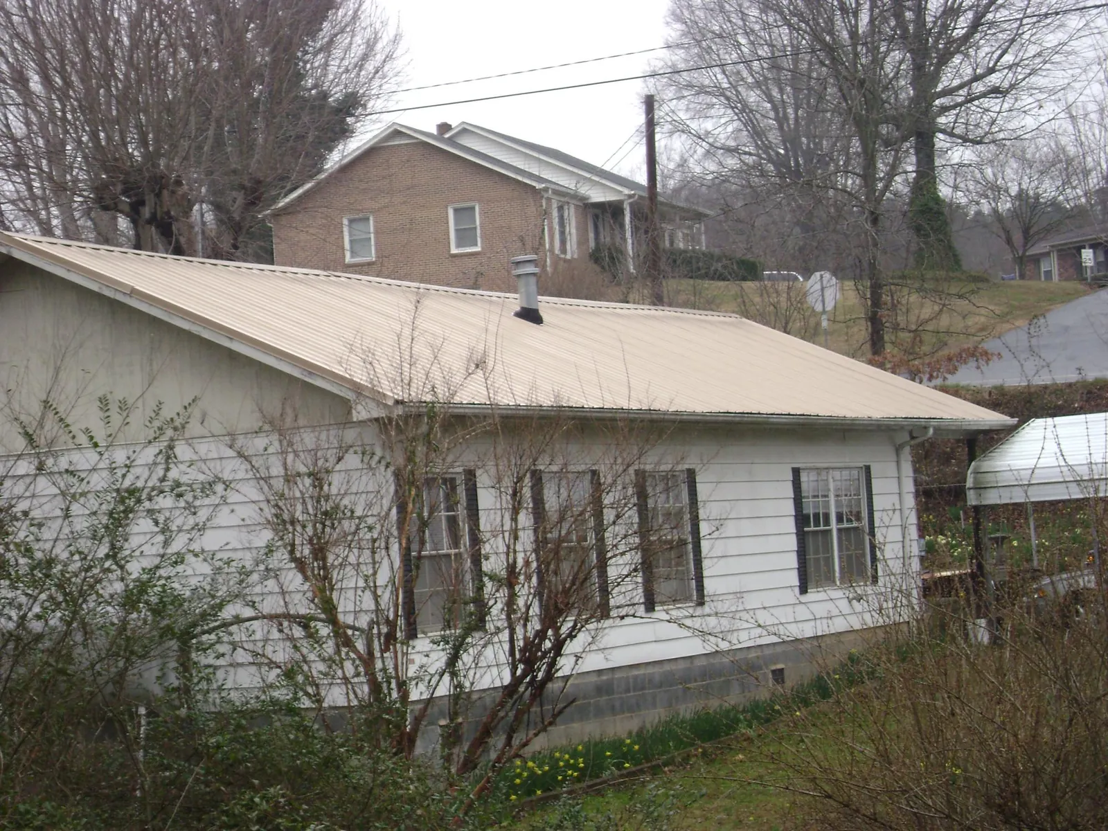 Tan metal roof on a white sided house set into a hillside — Commercial Roofing by Roofing Brothers in Colerain