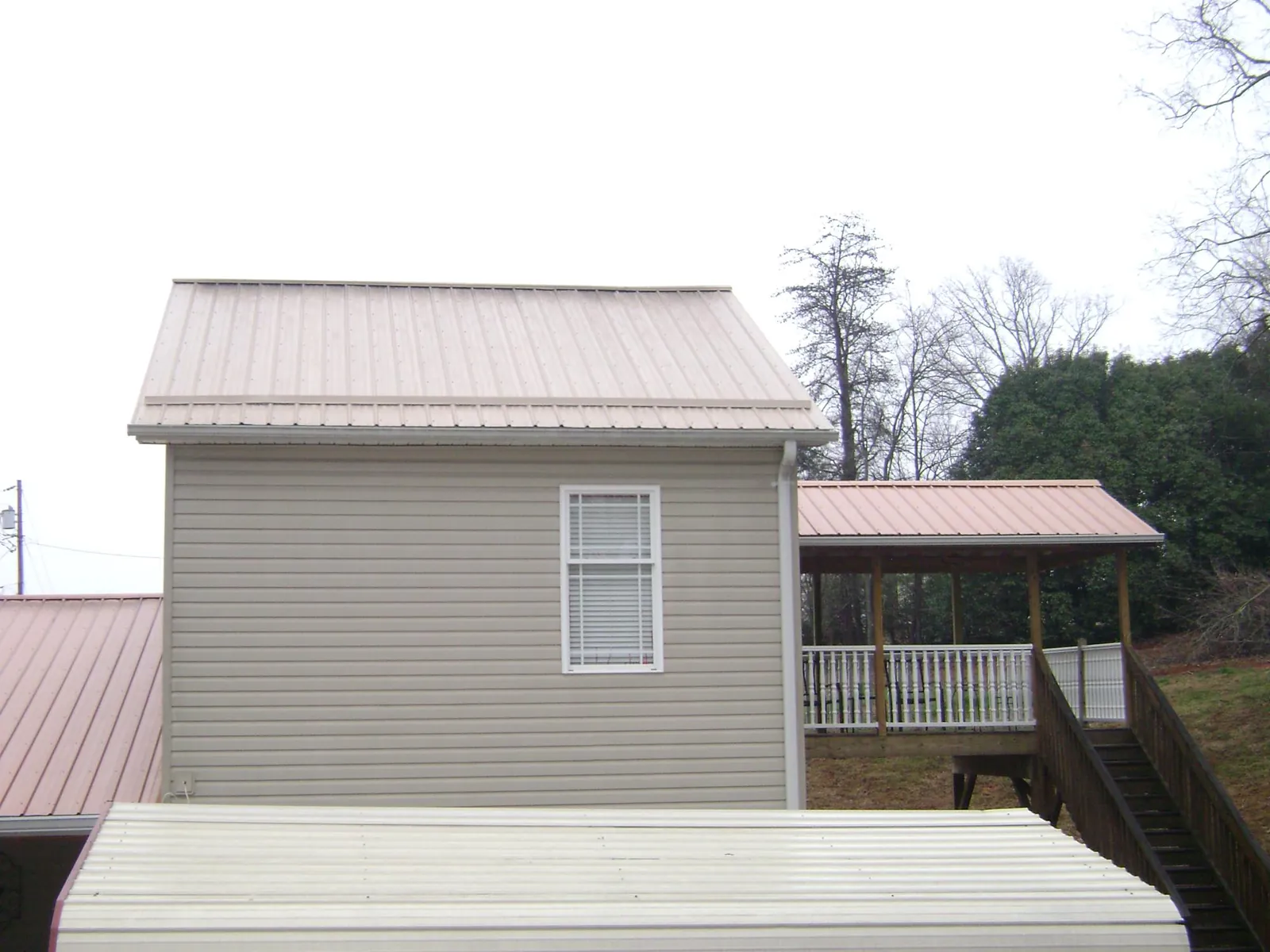 Tan metal roofs on a two story addition and attached porch, from a Roof Replacement job in Colerain